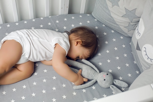 Baby boy lying in a round bed with a knitted rabbit toy