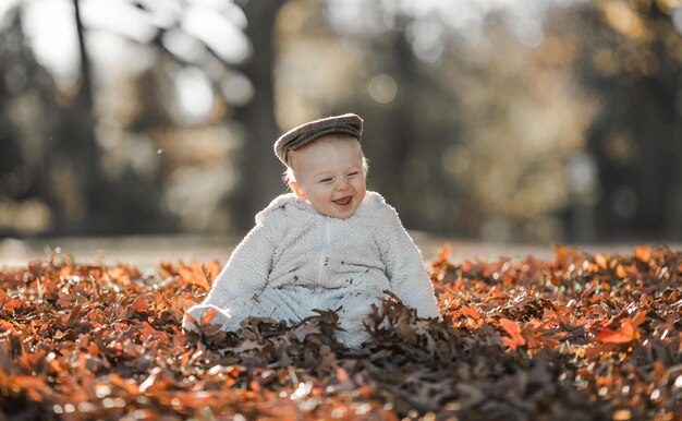 Foto bambino che gioca nel parco d'autunno bambini che lanciano foglie gialle bambino con foglie di quercia e acero fogliame autunnale