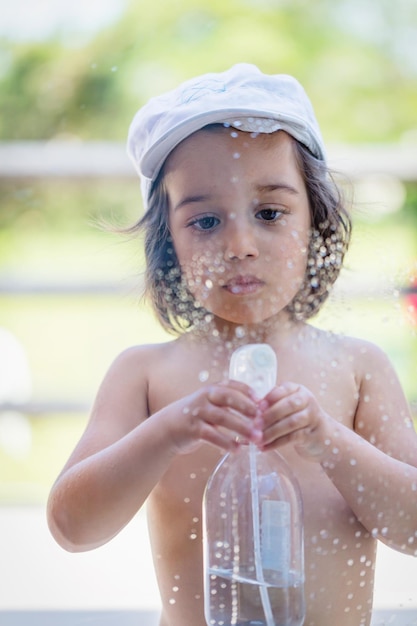 Photo baby boy playing outdood near window with spray bottle and water