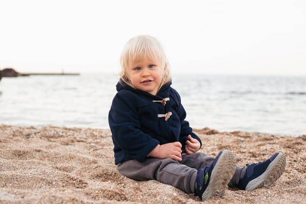 Baby boy playing on sand on beach in autumn time