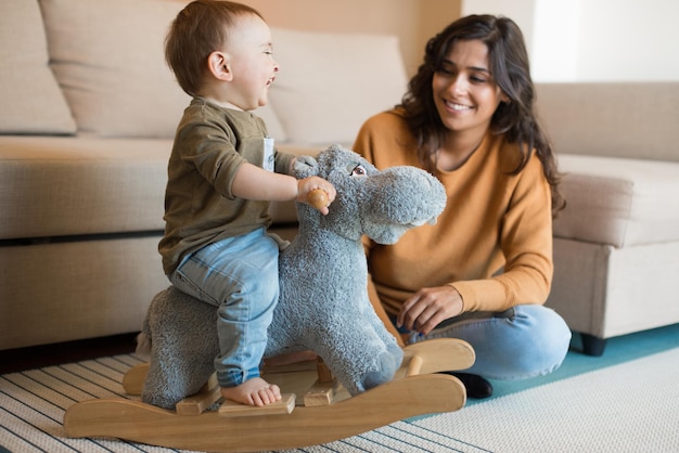 Baby boy playing with a rocking horse with mom's help