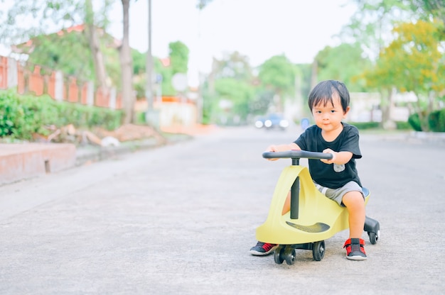 トライサイクルに乗る男の子。裏庭でトロカーに乗る小さなアジアの男の子。