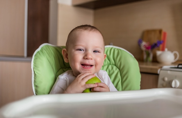 Baby boy sits in a chair and eats green apple