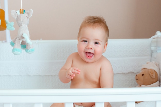 Baby boy sitting in a baby cot in a diaper