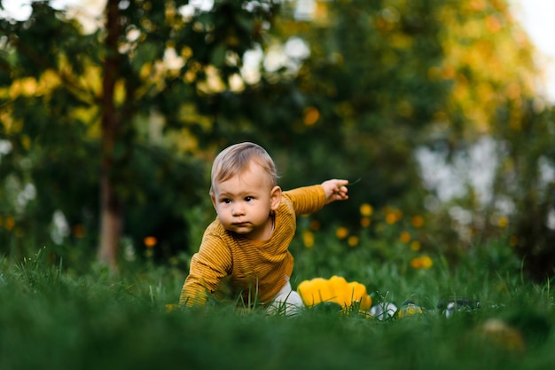 Baby boy sitting on the grass in summer day Child in trendy and cute clothes