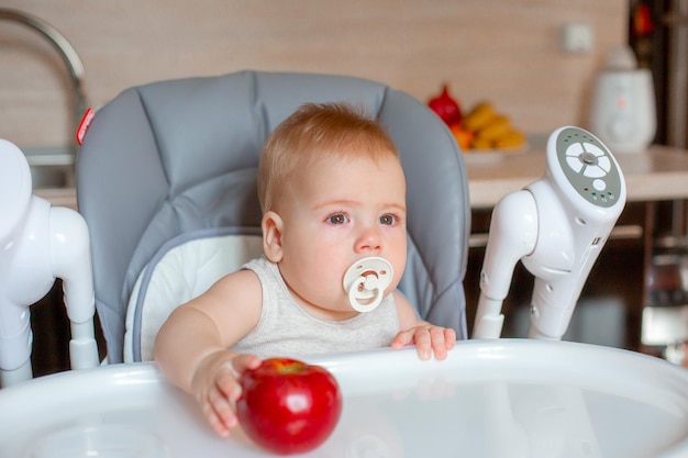 Baby boy sitting in the nursery eating an apple in the kitchen