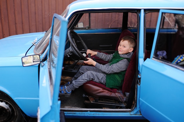 Baby boy sitting behind the wheel of a blue retro car and smiling