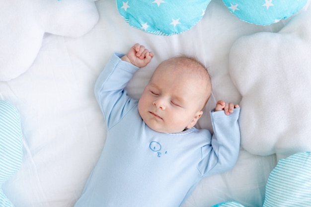 baby boy sleeps on the bed lying on his back among the pillows in blue pajamas, healthy newborn sleep