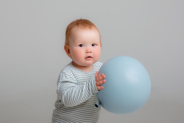 Baby boy stands holding a balloon on a white background