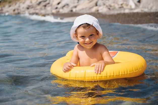 Baby boy swims with an inflatable yellow circle in the sea on a sunny day The kid learns to swim and enjoys the game