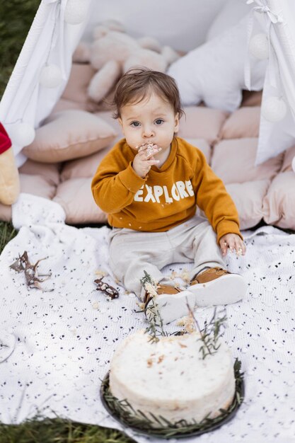 Photo baby boy tasting his birthday cake while sitting in wigwam