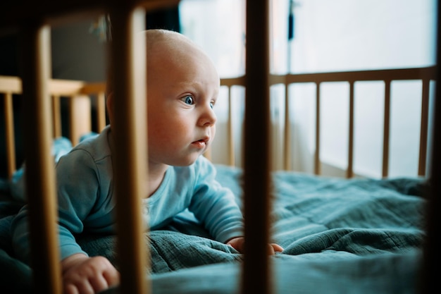 Baby boy toddler crawling in crib at kids nursery room at home looking and smiling at the camera