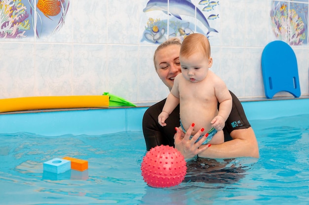 Baby boy trains to swim in the pool with a trainer