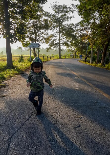 Foto bambino che cammina sulla strada in mezzo agli alberi