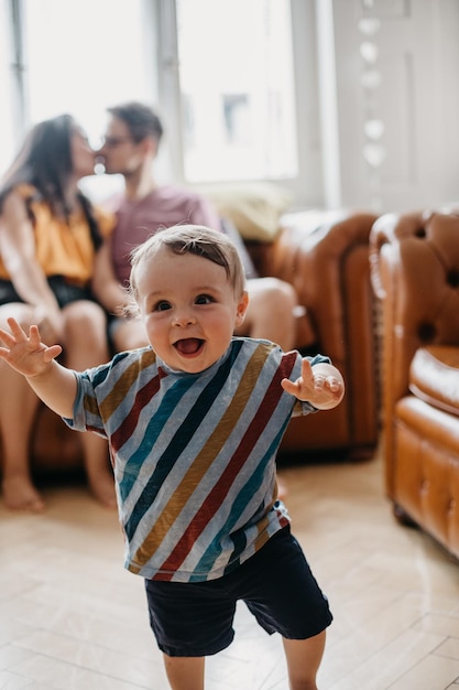 baby boy walking while parents kissing on sofa at home
