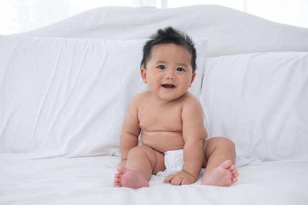 Baby boy wearing diaper in white sunny bedroom