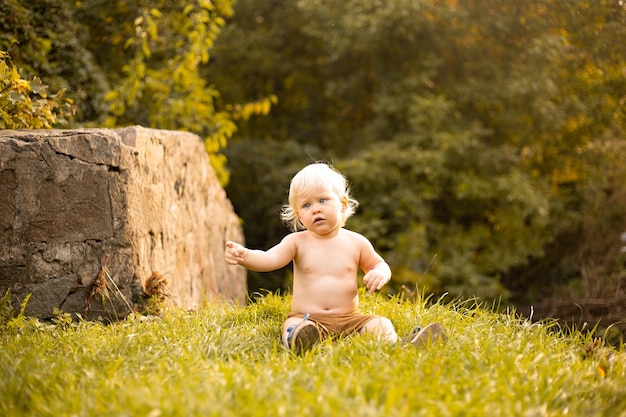 Baby boy wearing shorts in autumn or summer park with golden and green trees