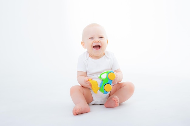 Baby boy in a white bodysuit is sitting playing with toy cars on white background