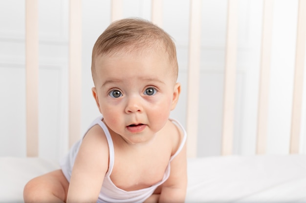 Baby boy in white clothes sitting in a crib