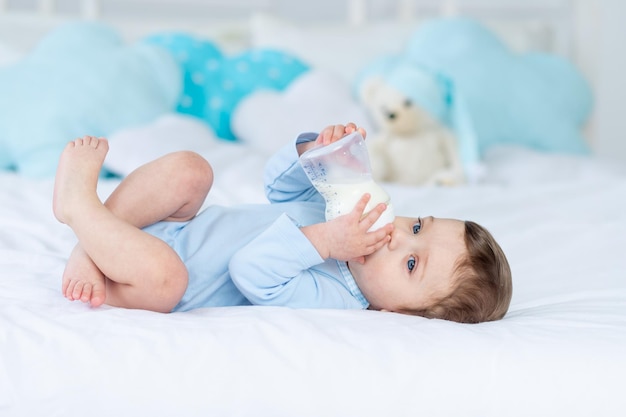 Baby boy with a bottle of milk on the bed for sleeping in a blue bodysuit baby food concept