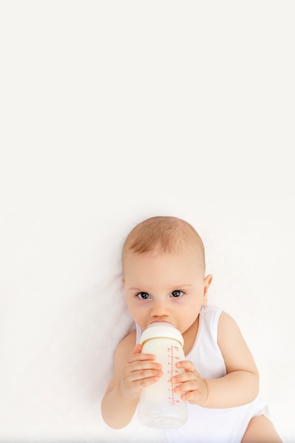 Baby boy with a bottle of milk on a white bed at home