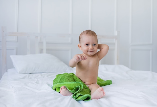 A baby boy with brown eyes sits on the cotton bedding on the bed and looks at the camera