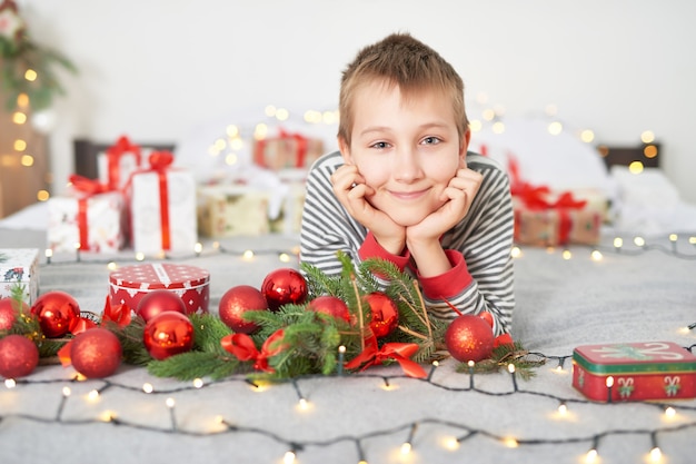 クリスマスの装飾が付いているベッドの上の自宅でクリスマスプレゼントと男の子