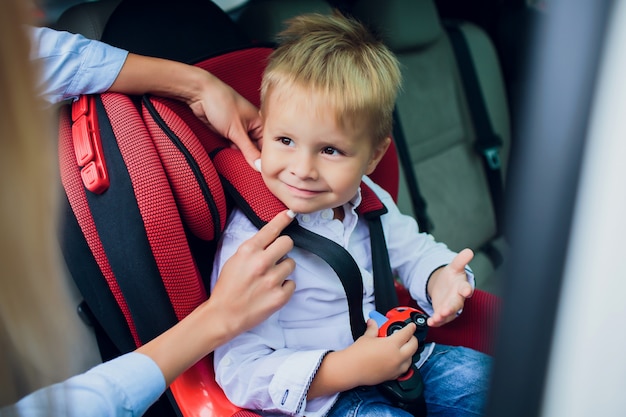 Neonato con i capelli ricci seduto nel seggiolino per bambini con auto giocattolo nelle mani