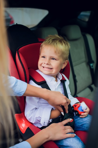 Baby boy with curly hair sitting in child car seat with toy car in hands