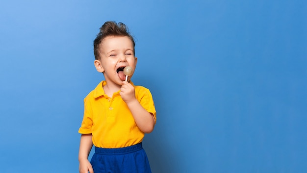 Baby boy with lollipop stands on a blue wall background