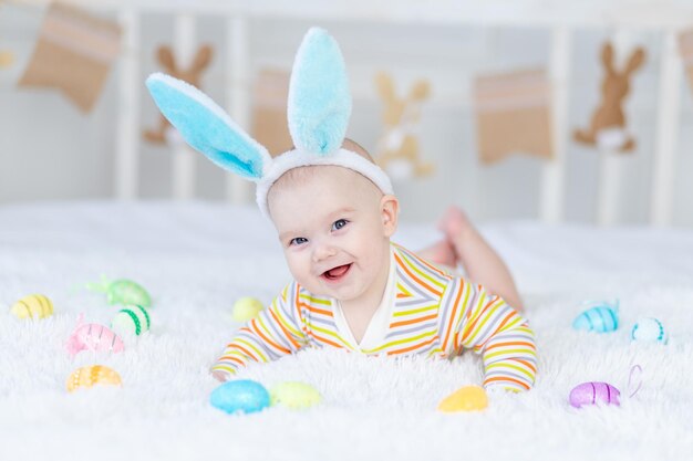 Baby boy with rabbit ears on his head lying on the bed with Easter eggs cute funny smiling little baby The concept of Easter