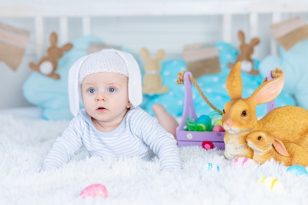 Ребенок в шляпе кролика на кровати с пасхальными яйцами и кроликами, концепция счастливой Пасхи