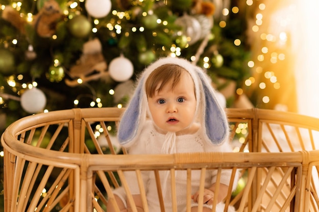 baby in a bunny suit in a crib on the background of the Christmas tree