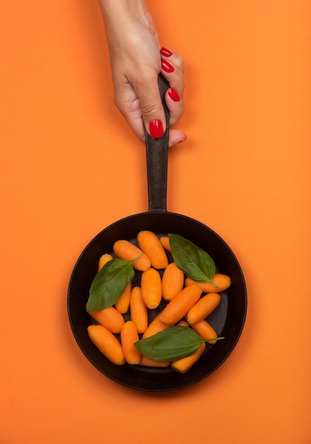 Baby carrot on the frying pan on orange background