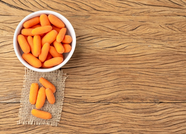 Baby carrots in a bowl over wooden table with copy space