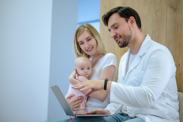 Baby check-up. Blonde jonge vrouw met een baby in gesprek met een kinderarts in de kliniek