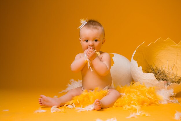 Bambino in un costume di pollo con piume e uova di pasqua su una parete arancione, spazio per il testo. il concetto di pasqua