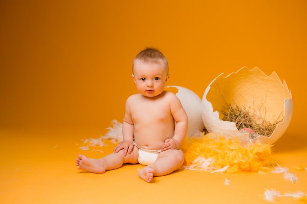 Baby in a chicken costume with feathers and easter eggs on a orange wall, space for text. the concept of easter