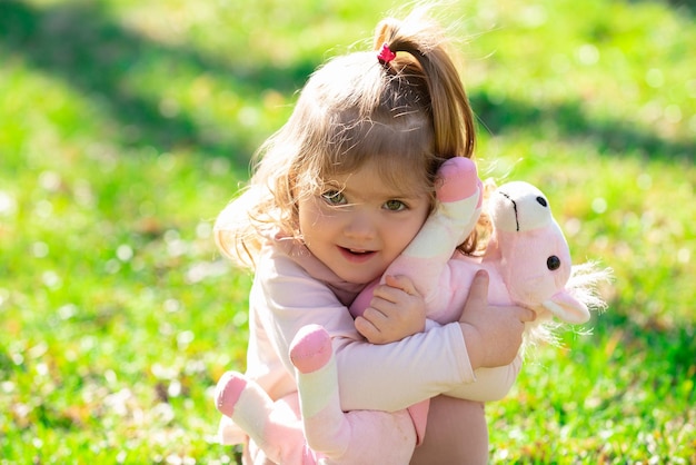 Baby child hug toy in green grass on spring lawn Little kids walking in the park