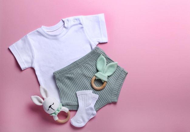 Photo baby clothes and accessorizes on pink background top view copy space flat lay white tshirt green sh