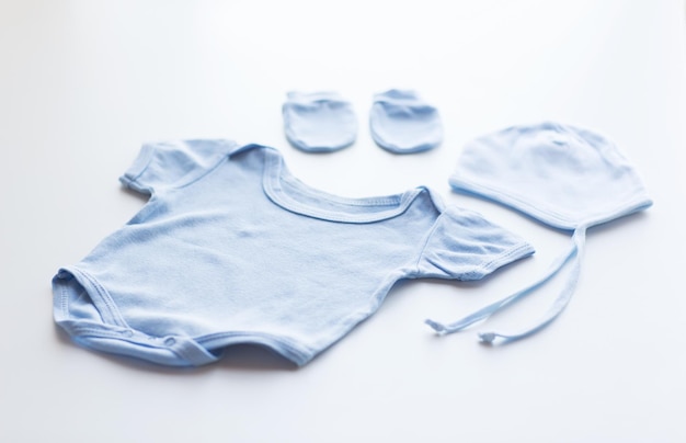 baby clothes, babyhood, motherhood and object concept - close up of blue bodysuit, hat and mittens for newborn boy on table