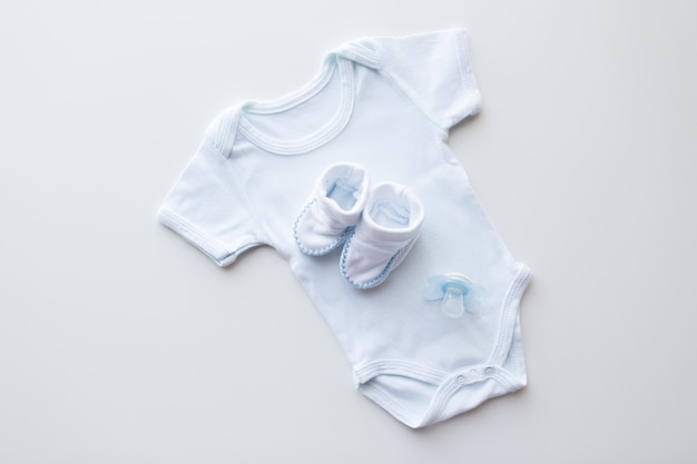 baby clothes, babyhood, motherhood and object concept - close up of white bodysuit, bootees and soother for newborn boy on table