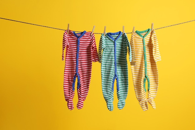 Baby clothes hanging on rope on yellow background