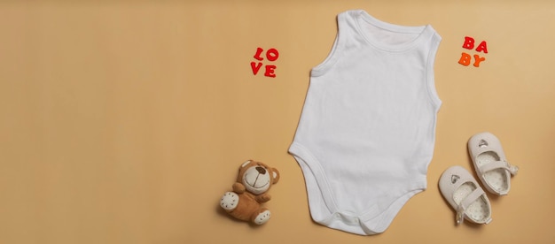 Photo baby clothes mockup template blank white jumpsuit for newborns shoes and teddy bear on beige background space for text top view banner