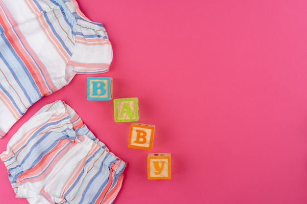 Baby clothes on pink background top view