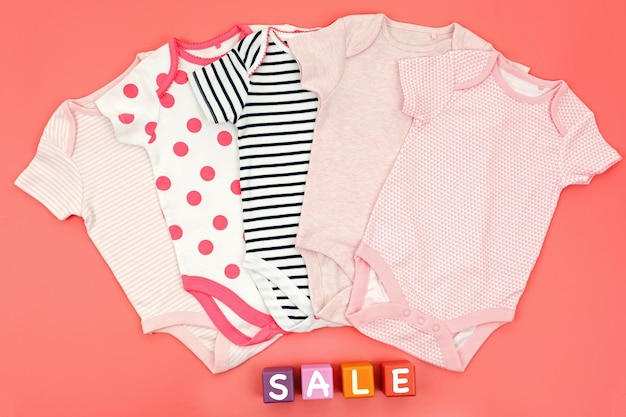 Baby clothes and wooden cubes on pink background Sale concept