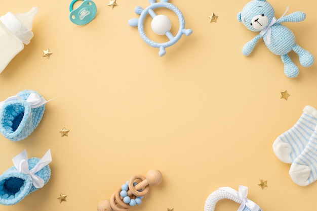 Baby concept Top view photo of blue teddybear toy rattle socks milk bottle teether soother knitted shoes and gold stars on isolated pastel beige background with empty space in the middle