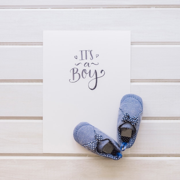 Baby concept with paper and pair of shoes on wooden surface
