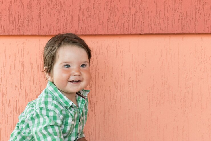 Baby on a coral wall. Little boy. in a checkered green and white shirt.