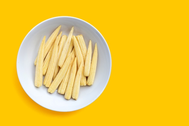 Baby corn in white plate on yellow background.